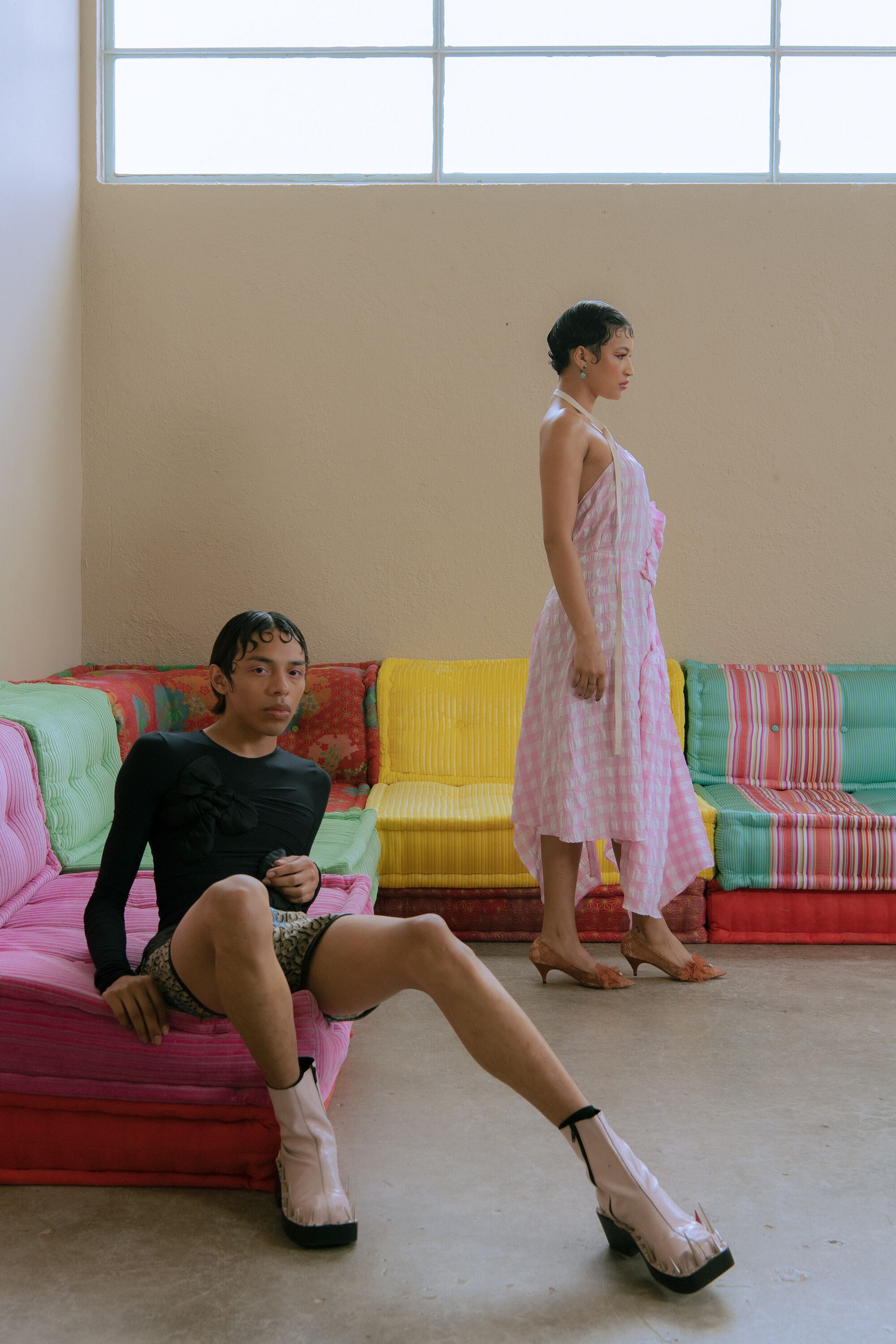 Una modella è seduta su un divano multicolore a forma di V, mentre un'altra è in piedi con un abito rosa.