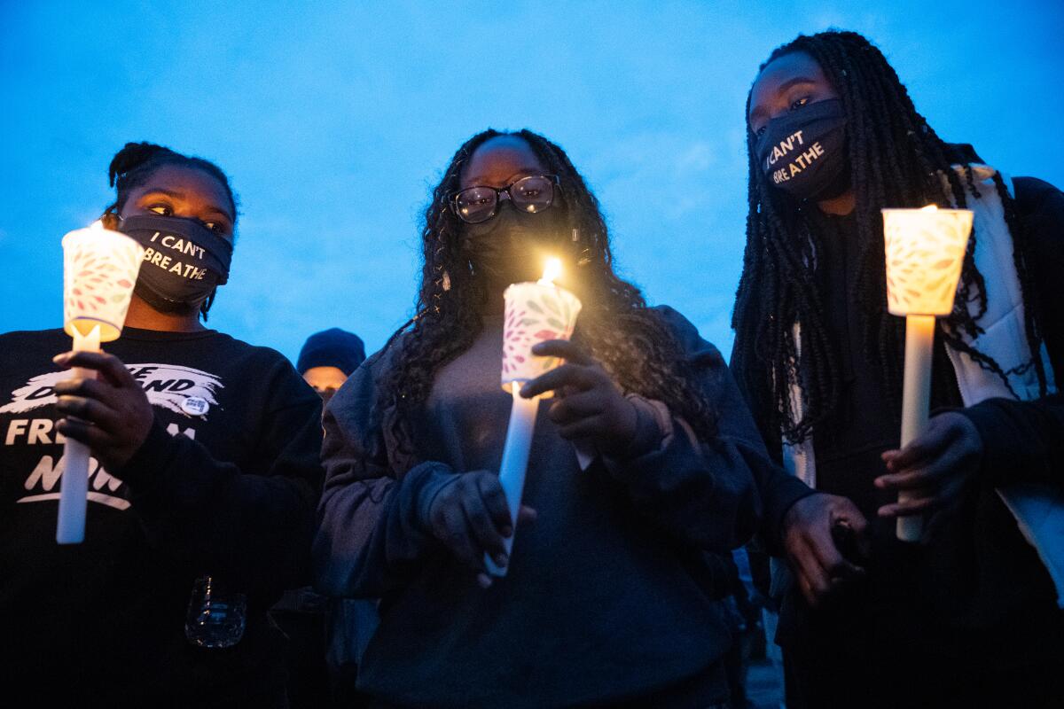 Three Black women hold candles during a protest for Daunte Wright outside the Brooklyn Center Police Department.