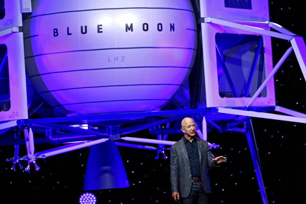 Jeff Bezos stands in front of a depiction of a spacecraft with the words "Blue Moon" on its side.