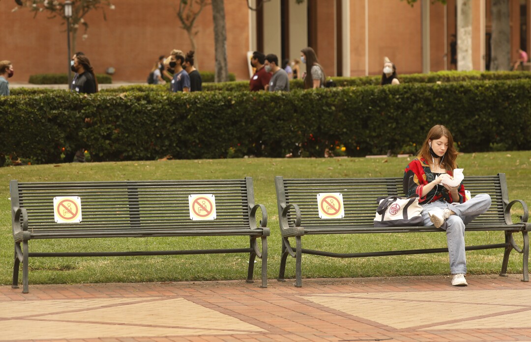 A female USC student eat lunch alone on a bench outside on campus.