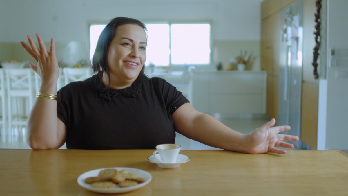 A woman at a kitchen table with a teacup and a plate of cookies.