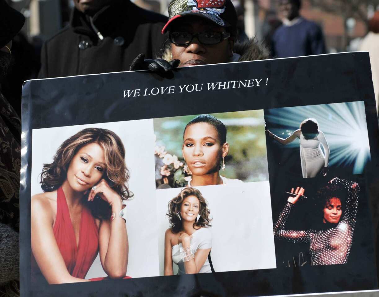 A woman holds a poster as the public gathers on the streets of Newark, N.J., near Whitney Houston's private funeral.