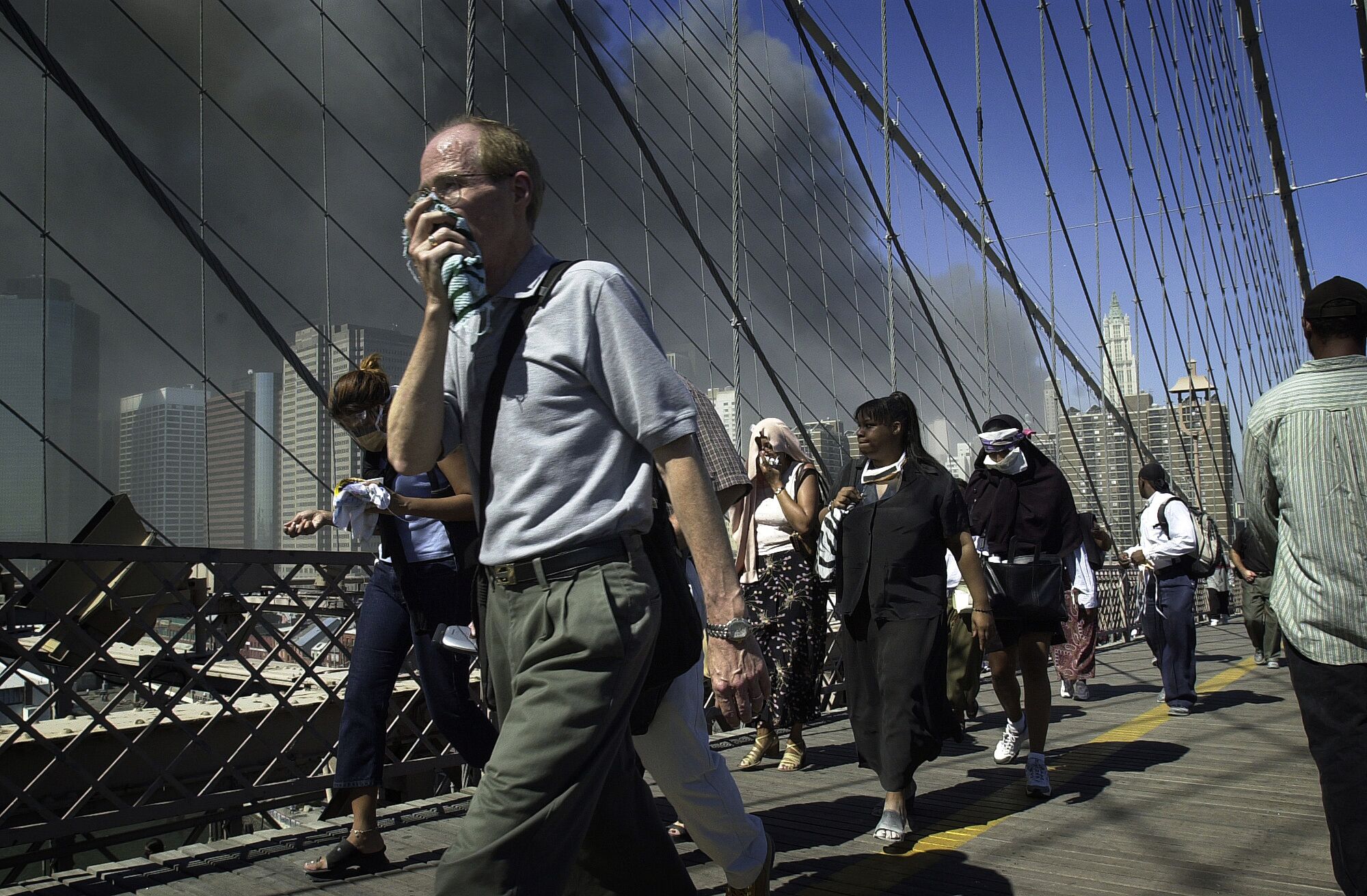 People walk over Brooklyn Bridge, smoke billowing in the background