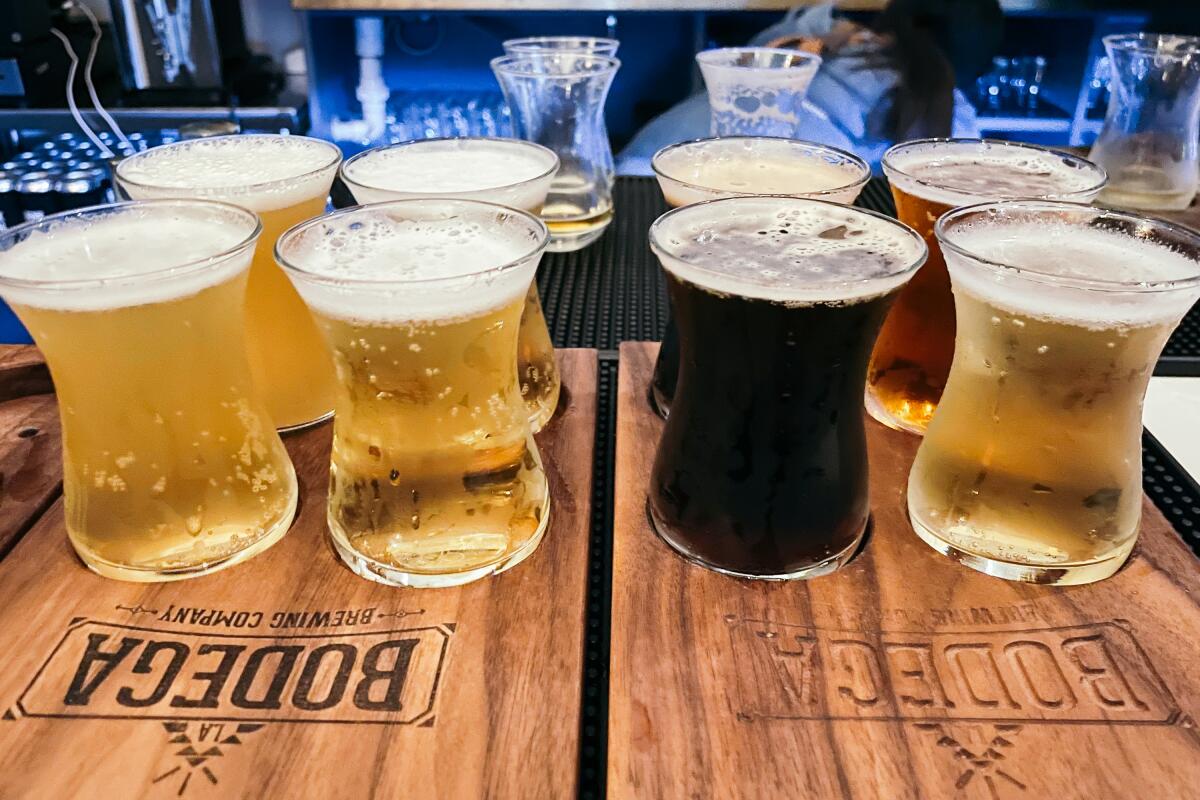 Two flights of 4 beer tasters side by side on wooden boards that say "LA Bodega Brewing Company"