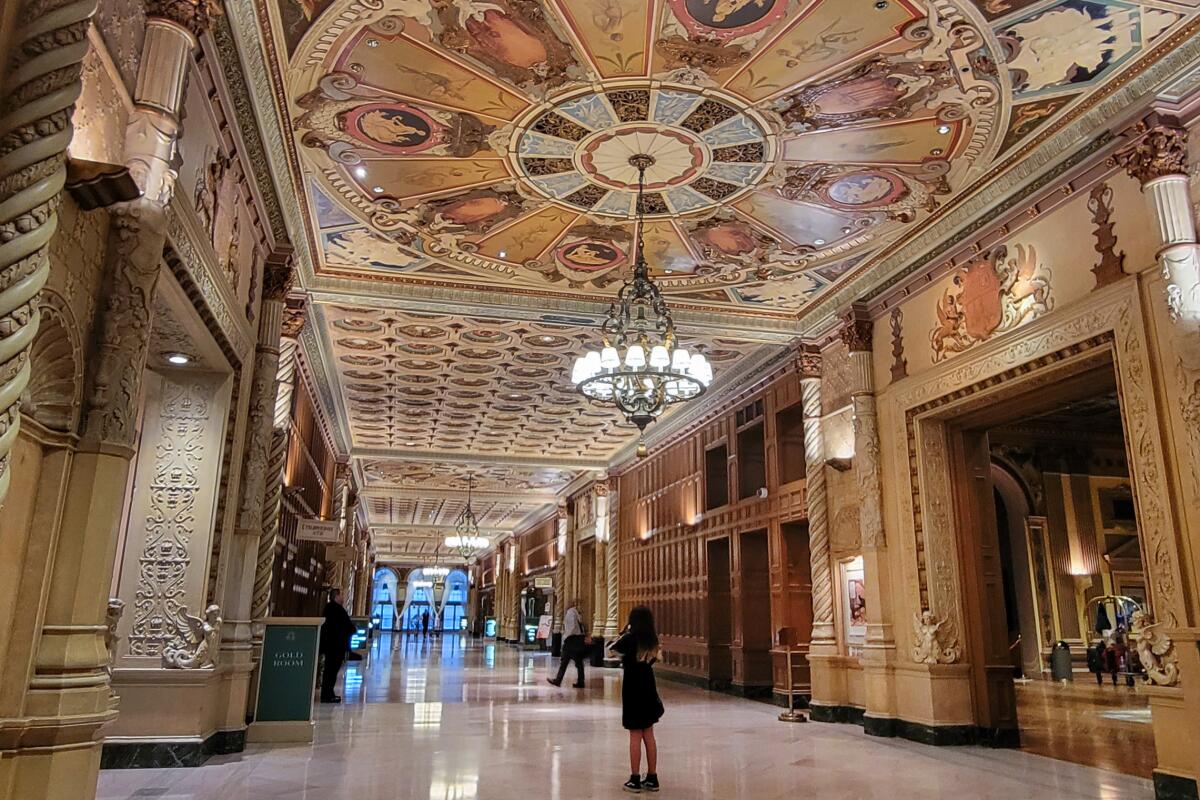 The grand lobby of the Millennium Biltmore Hotel in downtown Los Angeles, with tan and bronze mosaics and a deco chandelier.