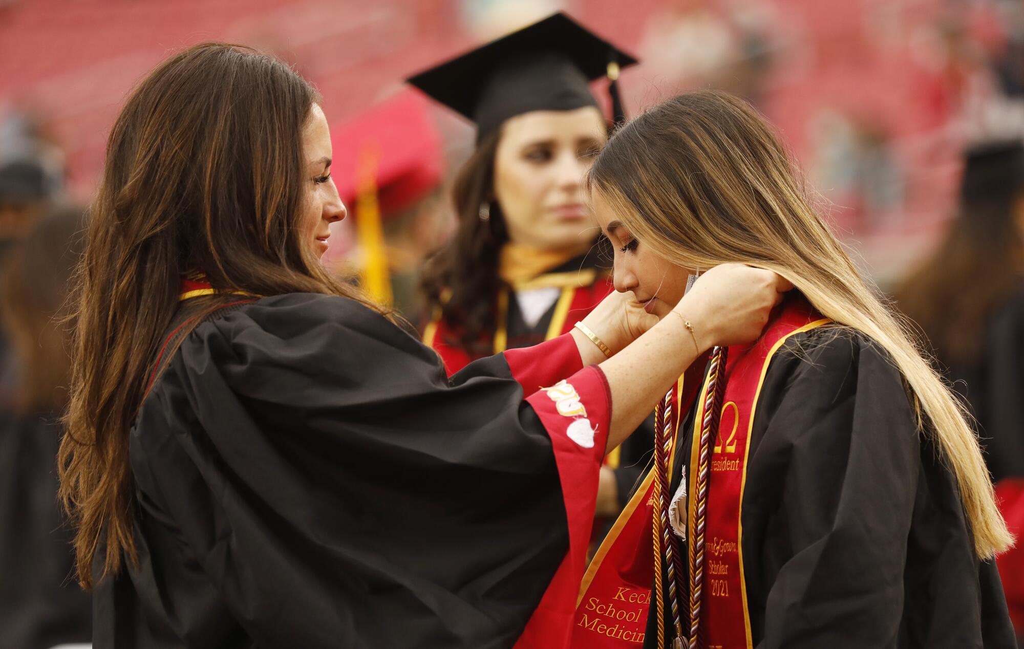 A woman adjusts the red sash around the neck of a fellow graduate