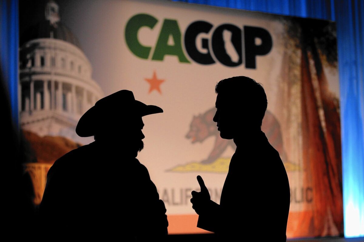 Two people talk in front of a "CA GOP" sign