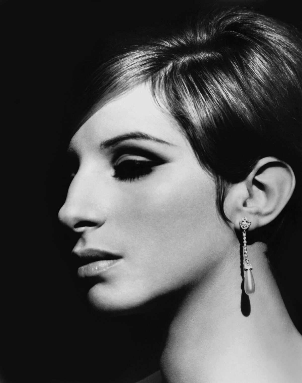 A side view of a woman with short hair, an earring and heavy eye makeup.