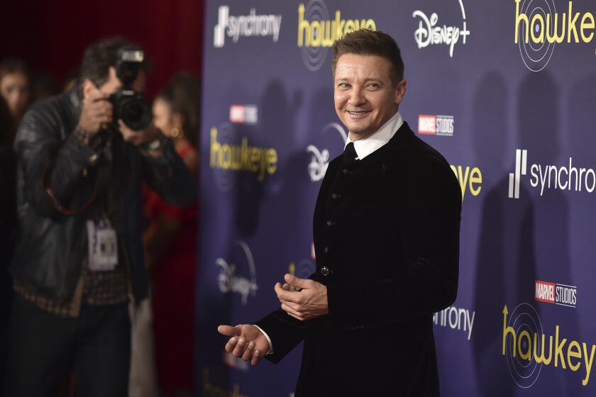 Jeremy Renner in a sweater and white collared shirt posing at a red carpet event