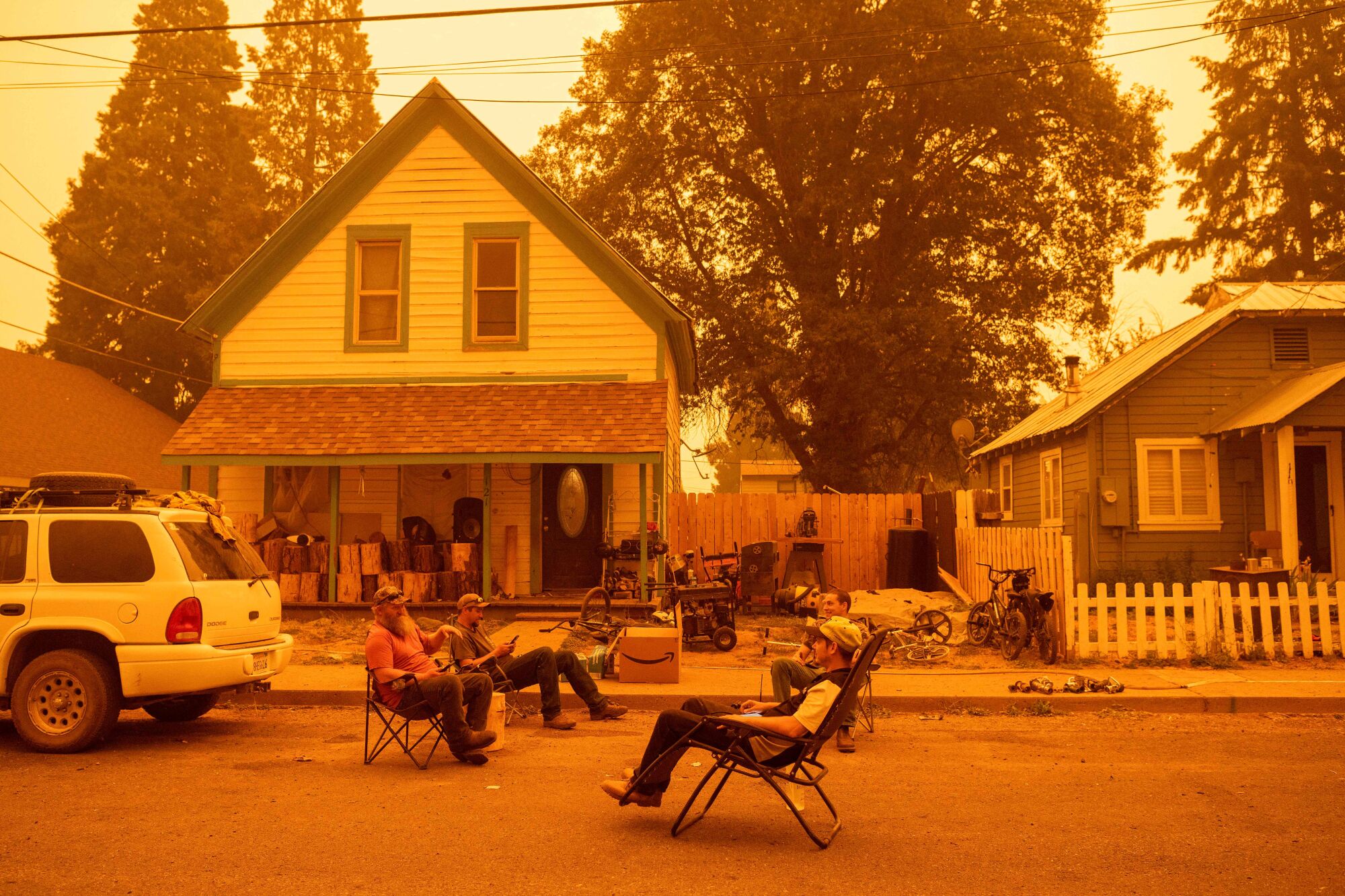 Residents sit in chairs in the street beneath an orange sky.