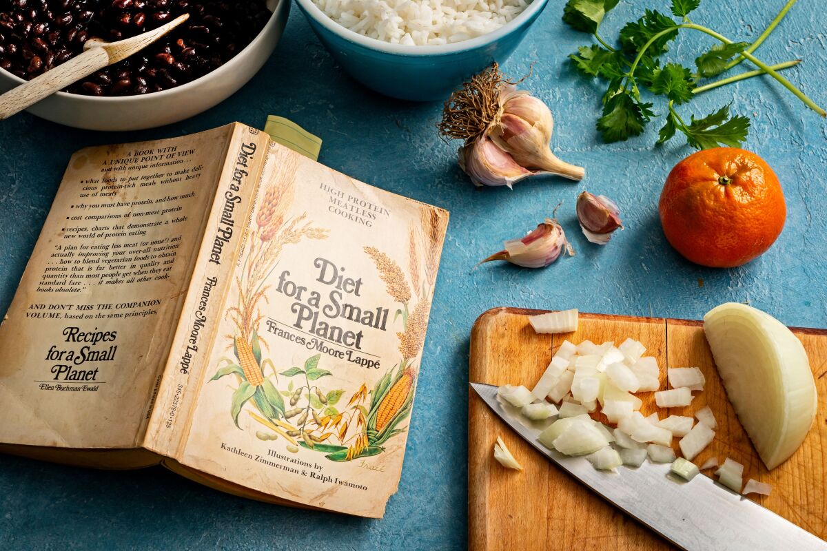 A well-used copy of "Diet for a Small Planet" sits open near a cutting board, knife and ingredients for a black bean stew.
