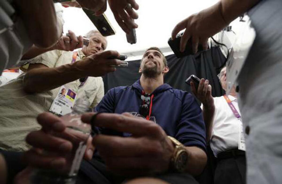 Michael Phelps is surrounded by reporters during a pre-Olympics news conference in London.