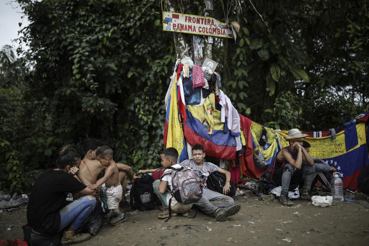 Migrants sit under a sign marking the Panama-Colombia border.