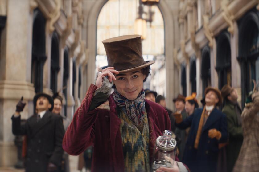 Timothée Chalamet tips his brown top-hat and smirks in front of a crowd of people looking skyward.