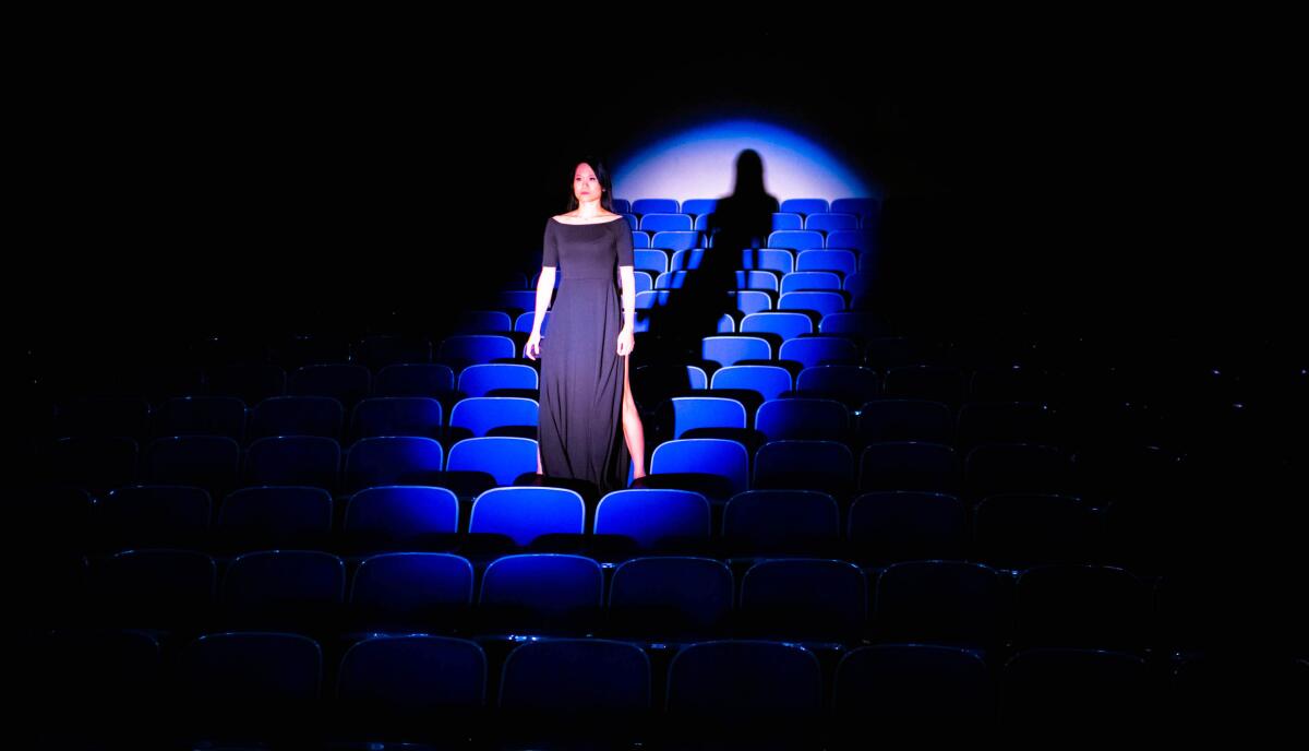 A woman stands on top of seats in a theater with a spotlight on her