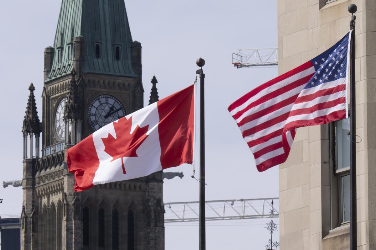 The Canadian and U.S. flags fly near a clock tower
