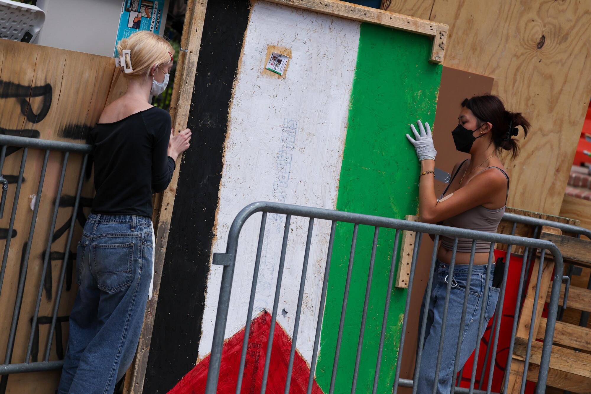 Two protesters wearing masks move a wood panel painted with the colors of the Palestinian flag