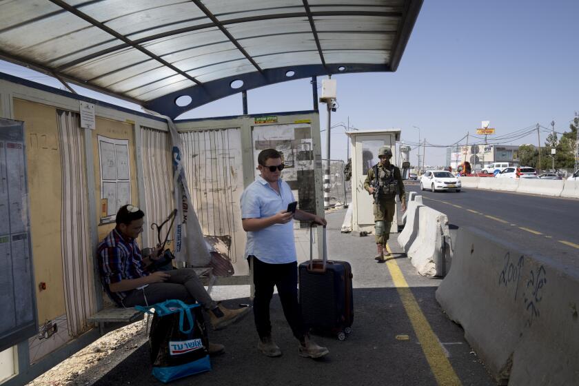 An Israeli soldier patrols a bus stop as settlers wait for a ride at the Gush Etzion junction, the transportation hub for a number of West Bank Jewish settlements, Thursday, June 9, 2022. Israeli settlers in the occupied West Bank may soon have a taste of the military rule that Palestinians have been living under for 55 years. A looming end-of-month deadline to extend legal protections to Jewish settlers has put Israel’s government on the brink of collapse and drawn widespread warnings that the territory could be plunged into chaos. (AP Photo/Maya Alleruzzo)
