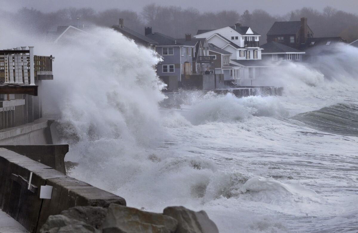Ocean waves crash over a seawall and into houses along the coast in Scituate, Mass., Thursday, ahead of a winter storm that was bringing strong winds to coastal areas.