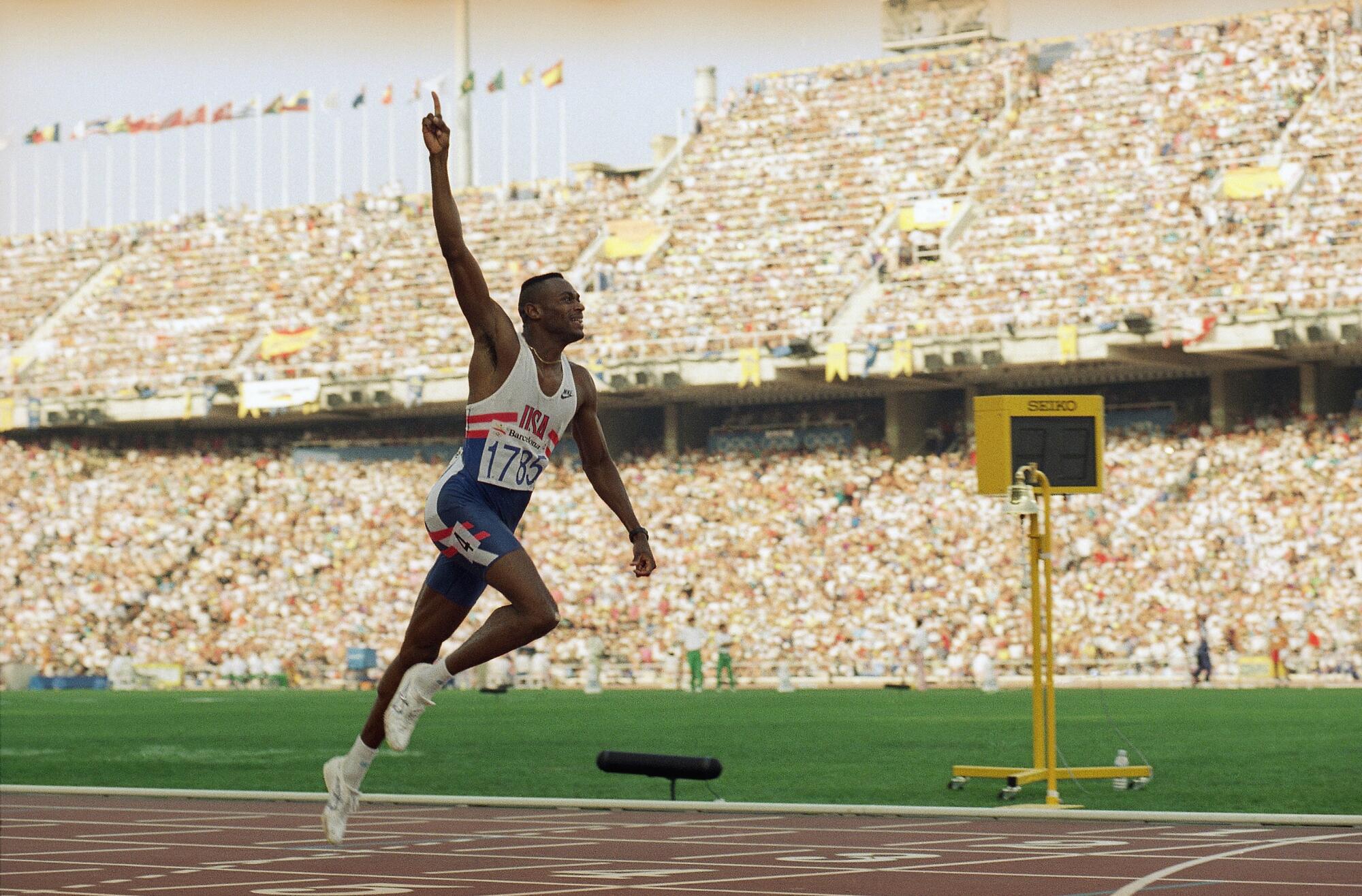 Kevin Young raises his right arm in victory as he wins the 400-meter hurdles in a world record time of 45.78 seconds.