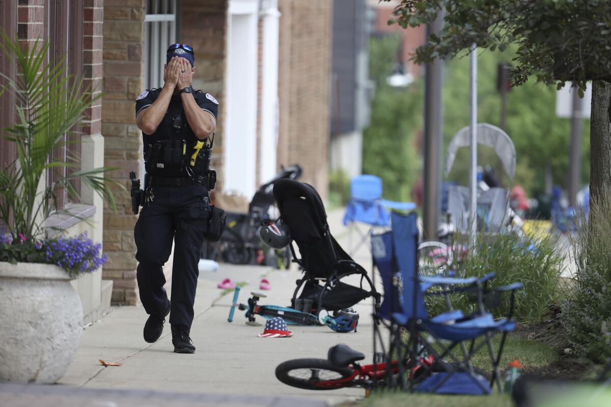 A police officer covers his face while walking through the scene after a Fourth of July parade shooting.