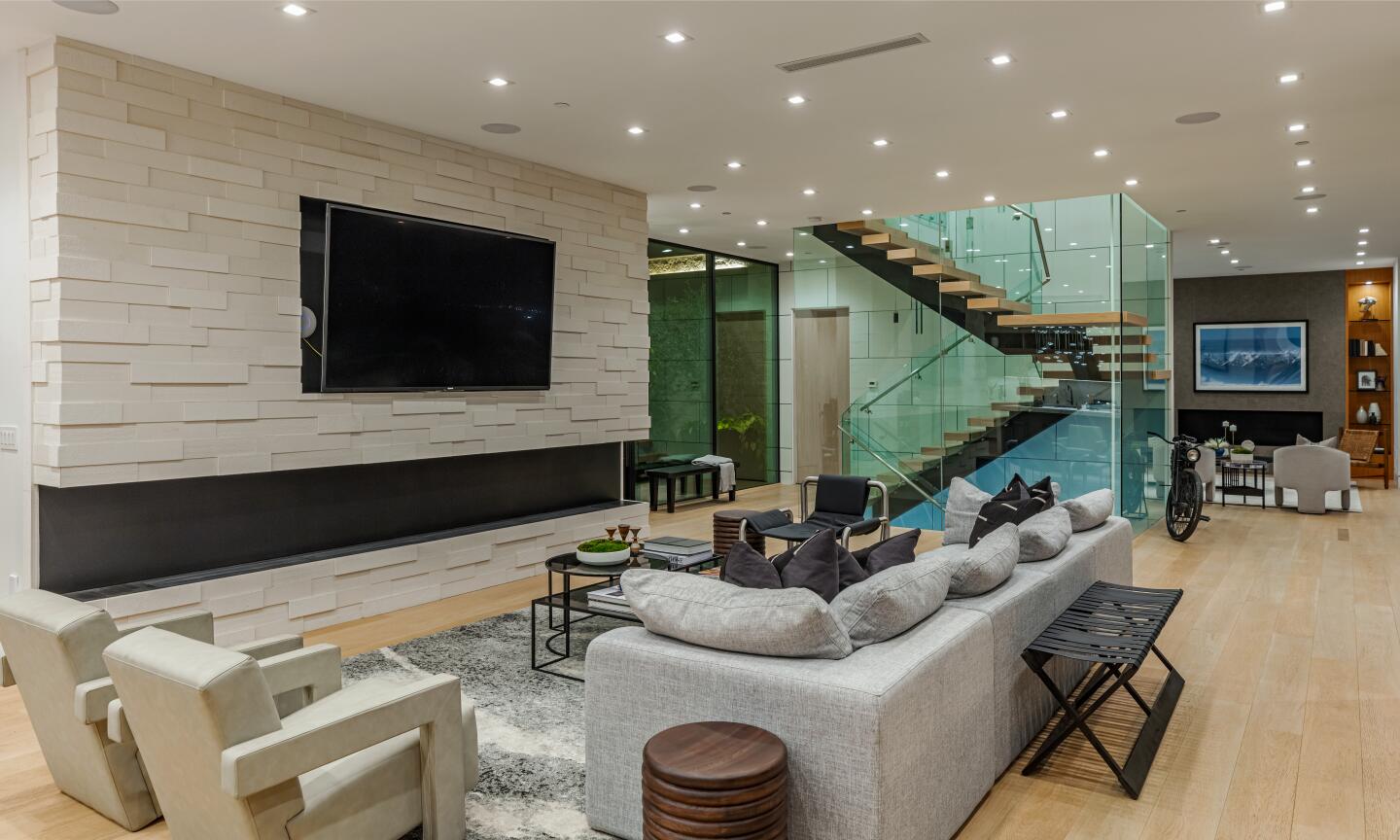 The living room has a built-in TV, furniture, a floating stairway and track lighting.