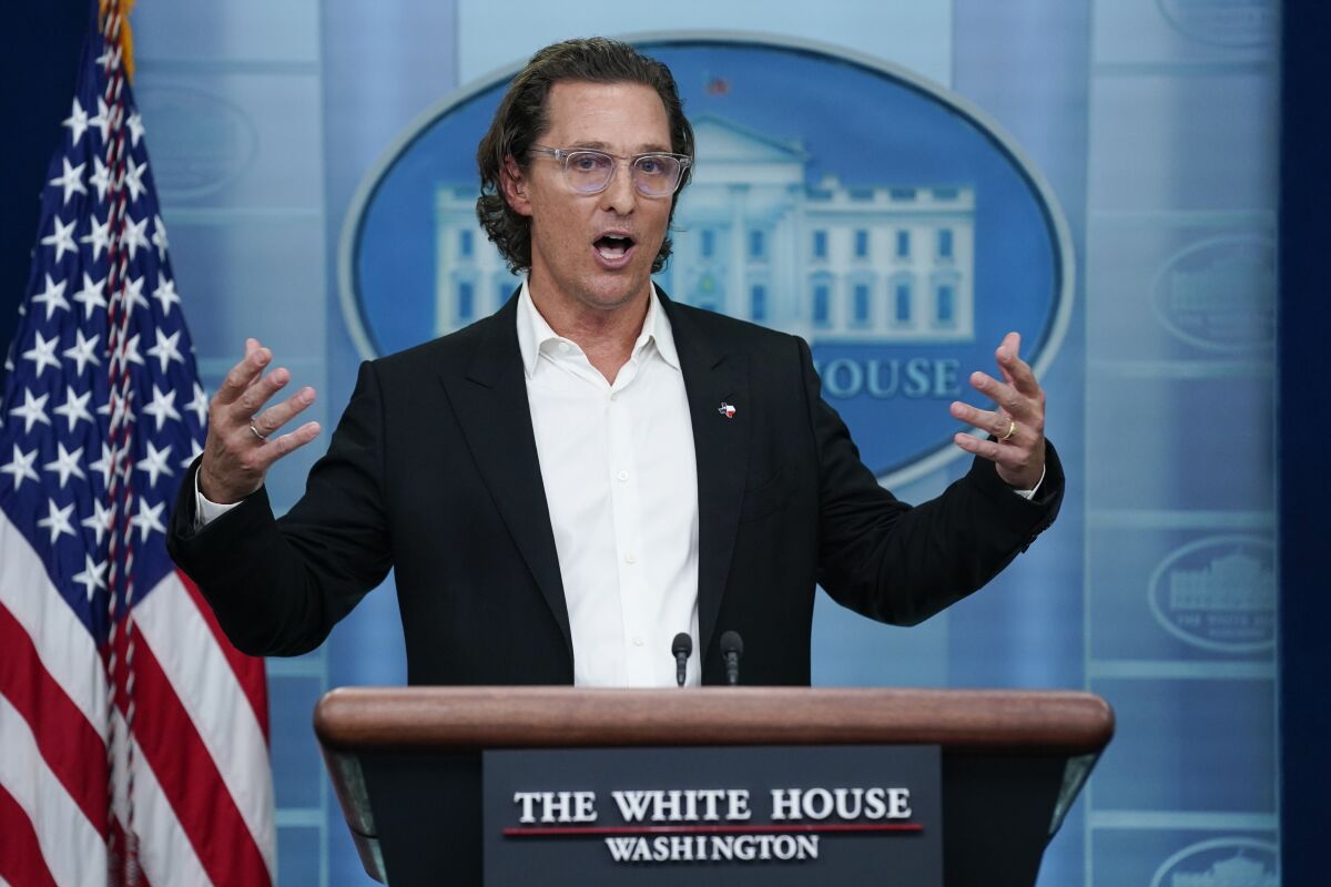 A man in glasses and a suit speaks in the White House briefing room with the American flag at his side