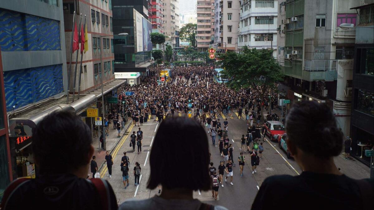 Bystanders watch from a footbridge June 16 as protesters march towards the government headquarters in Hong Kong Thursday.