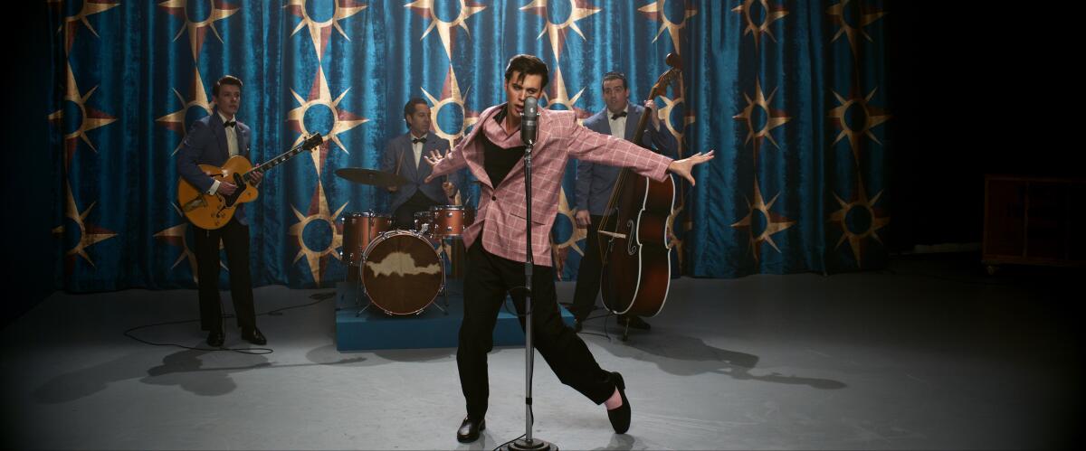 An actor portraying Elvis stands at a microphone with a swiveled hip.