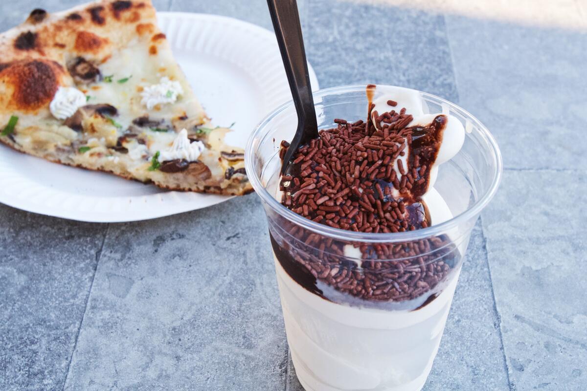 A slice of mushroom and ricotta pizza behind vanilla soft serve topped with chocolate syrup and sprinkles at Speak Cheezy