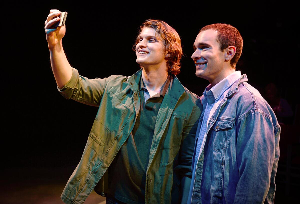 In a stage scene, two young men smile for a selfie