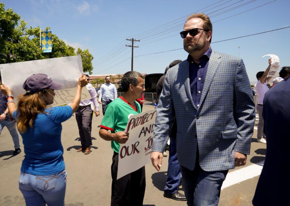 Doug O'Neill walks by protesters carrying signs.