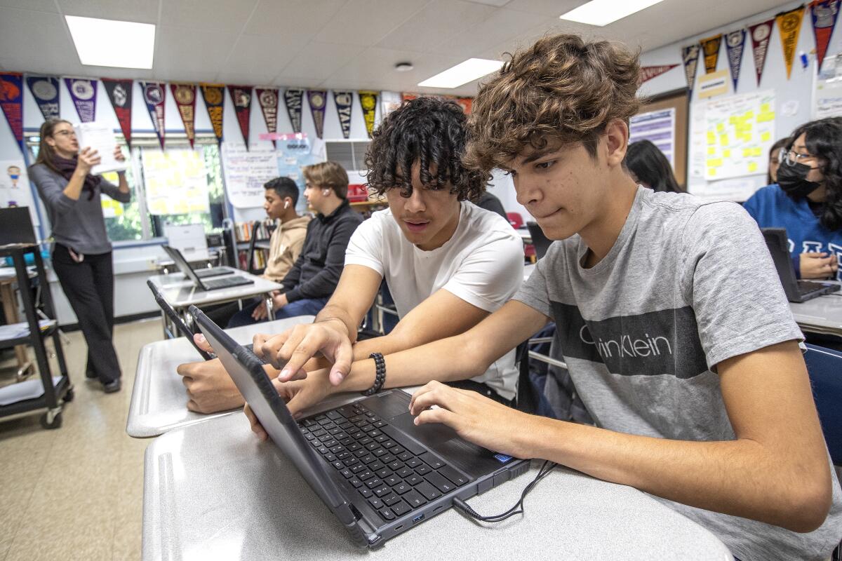 Seated in a classroom, teens look at laptops in class. 