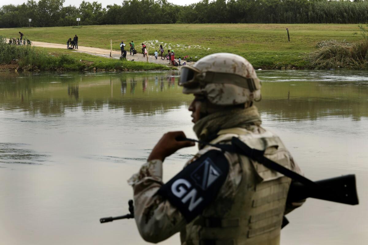 A member of the Mexican National Guard watches a group of migrants cross the Rio Grande to the U.S., where they will be picked up by Border Patrol.