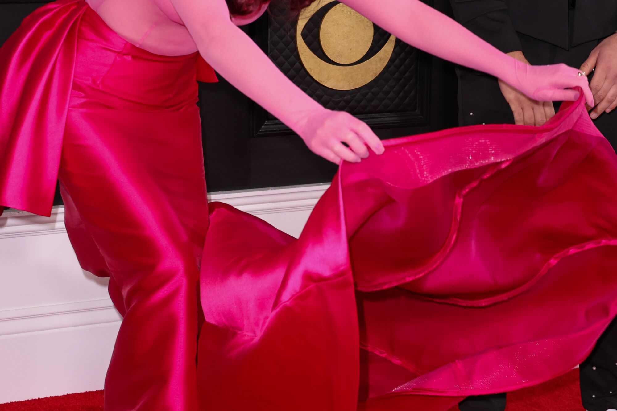Hands hold a long red train of a red and pink dress
