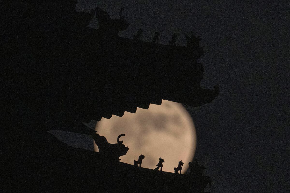 Roof decorations on the corner tower at the Forbidden City depicting sacred beasts are silhouetted against a supermoon, Tuesday, June 14, 2022, in Beijing. The moon reach its full stage on Tuesday, during a phenomenon known as a supermoon because of its proximity to Earth, and it is also labeled as the "Strawberry Moon" because it is the full moon at strawberry harvest time. (AP Photo/Ng Han Guan)