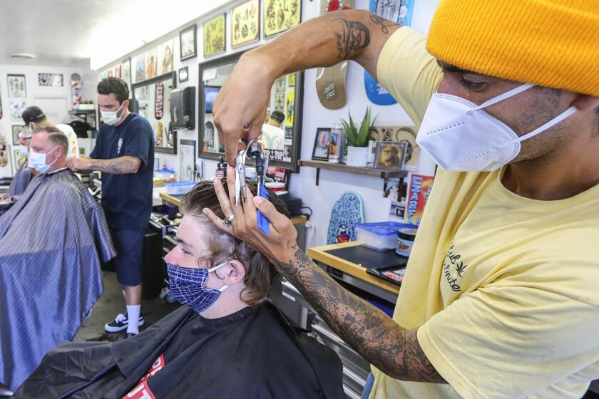 Leucadia Barber Shop manger Emiliano Zermeno (right) cuts the hair of Ben Canedy,13, on May 27, 2020 in Encinitas, California. This was the first day salons have been allowed to reopen since the shutdown.