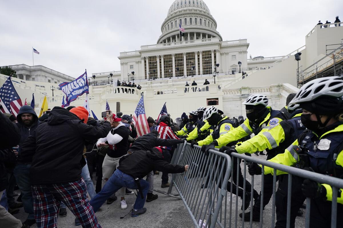 People, left, push at metal barriers as they face a line of officers in neon and black clothing near a white building