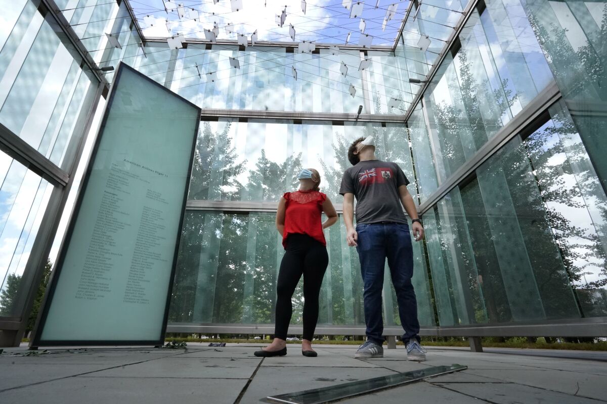 Chloe Taub and Anthony Brobenzano, of Hollywood, Fla., look at the 9/11 memorial at Logan International Airport, Thursday, Aug. 19, 2021, in Boston. The two were the only visitors during a three-hour span that afternoon. Tucked in a grove of ginkgo trees, the glass cube at Logan Airport pays tribute to those lost aboard the two jetliners that took off from Boston and were hijacked by terrorists who flew them into the World Trade Center towers. But it's mostly silent homage. The memorial etched with the names of those who perished aboard American Airlines Flight 11 and United Airlines Flight 175 draws few visitors. (AP Photo/Elise Amendola)