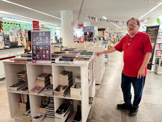 A man in a red shirt and black pants stands in a bookstore