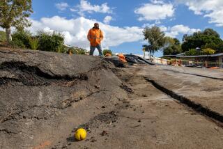 Rancho Palos Verdes, CA - February 09: A construction worker walks along cracked pavement where land movement exacerbated by recent storms has caused large cracks and damage to nearby homes in the 4300 block of Dauntless Dr. on Friday, Feb. 9, 2024 in Rancho Palos Verdes, CA. (Brian van der Brug / Los Angeles Times)