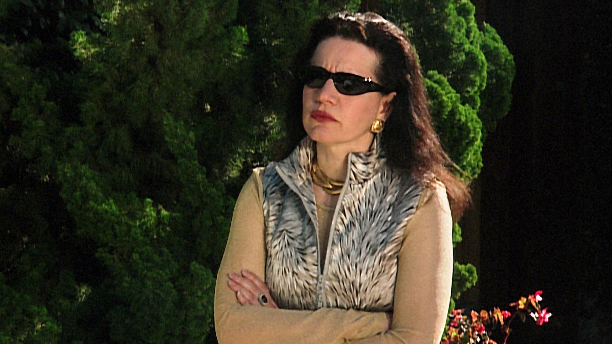 A woman in sunglasses and a zebra print vest standing angrily with her arms crossed.