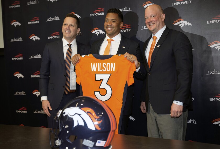 Russell Wilson holds up a jersey at a news conference with coach Nathaniel Hackett and GM George Paton.