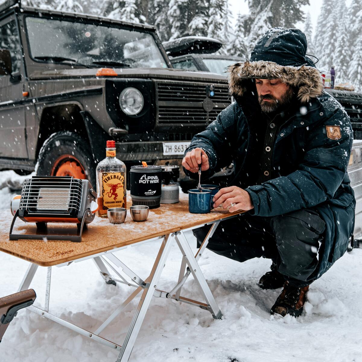 A man in the snow having a drink with his overland vehicle in the background.