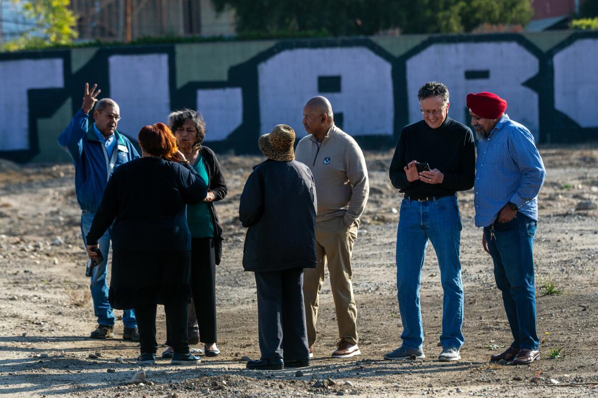 A group of people stand on a dirt lot.