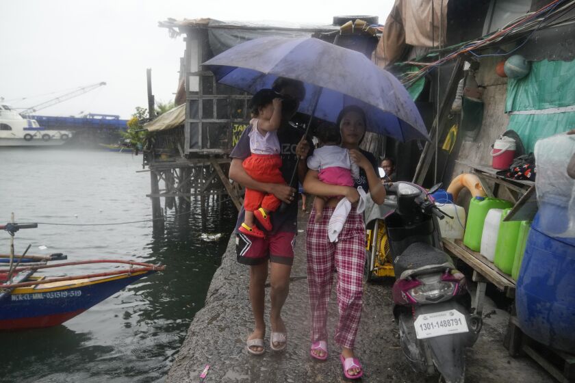 Residents carry their children as they evacuate to safer grounds to prepare for the coming of Typhoon Noru at the seaside slum district of Tondo in Manila, Philippines, Sunday, Sept. 25, 2022. The powerful typhoon shifted and abruptly gained strength in an "explosive intensification" Sunday as it blew closer to the northeastern Philippines, prompting evacuations from high-risk villages and even the capital, which could be sideswiped by the storm, officials said. (AP Photo/Aaron Favila)