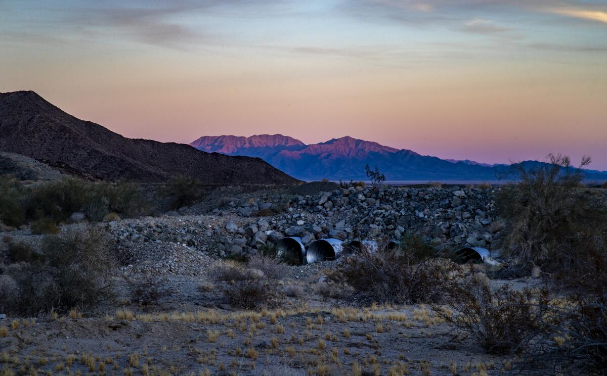 Water culverts run through a rocky berm in a desert area at twilight 