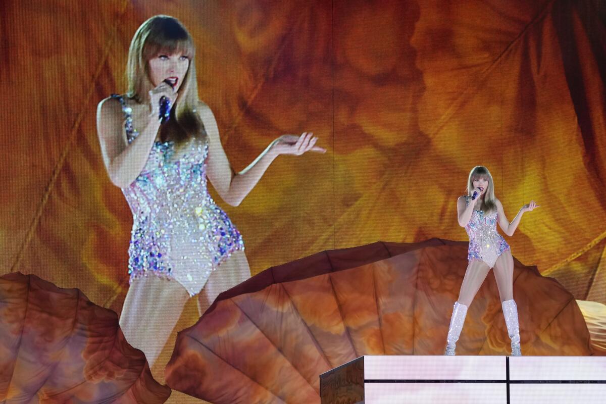 Taylor Swift performs onstage in a sequined bodysuit in front of a huge projection of herself.