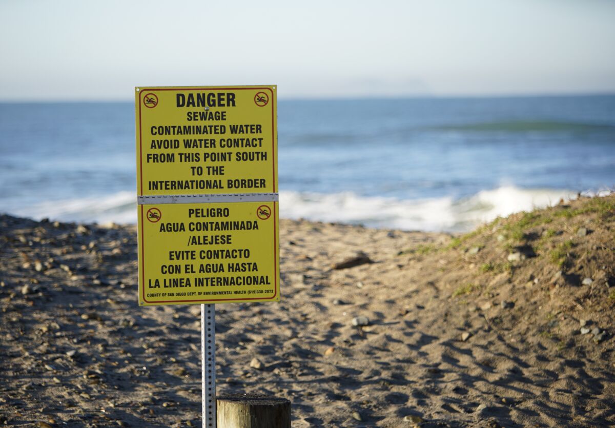 A sign on a beach reads "Danger - Sewage - Contaminated Water."