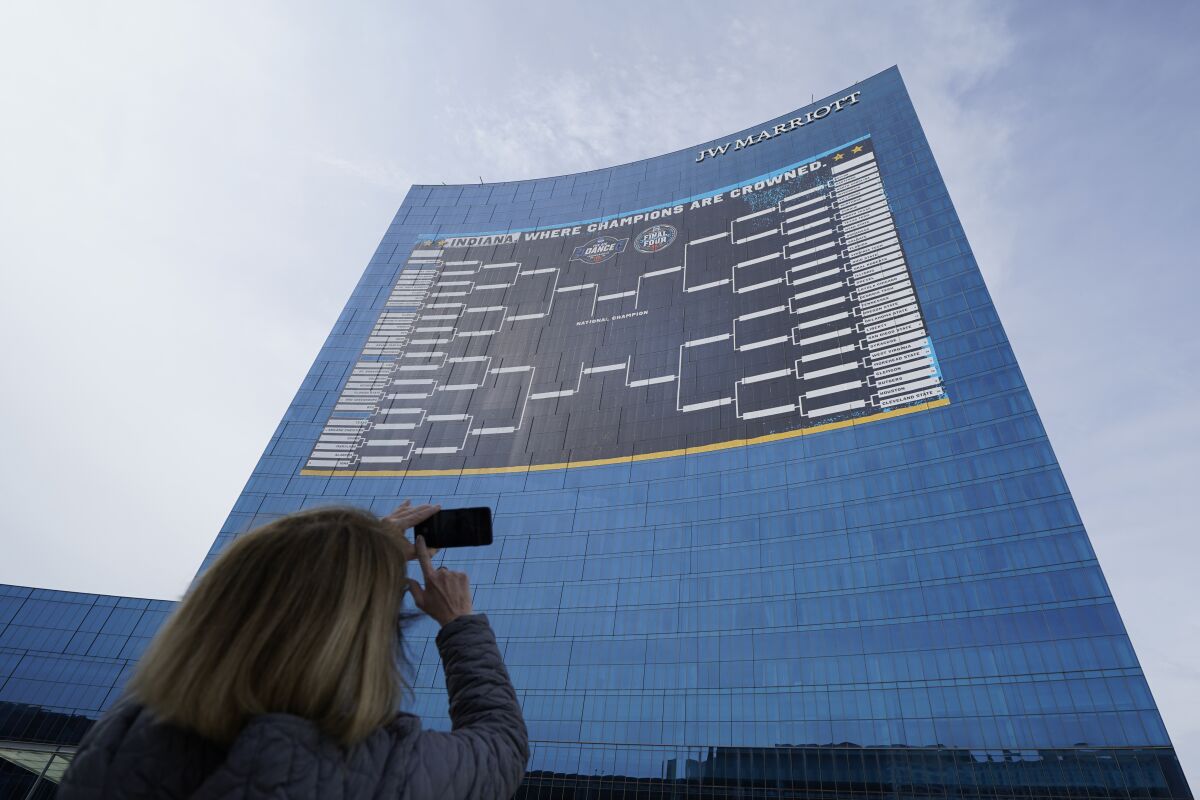 FILE - Lisa Moeller takes a photo of the NCAA bracket for the NCAA college basketball tournament on the side of the JW Marriott in downtown Indianapolis. Wednesday, March 17, 2021. Wagering on all those parlays and longshots on the betting app — fun. Filling out a bracket and waiting for the upsets to begin — that’s why they call this March Madness. (AP Photo/Darron Cummings, File)